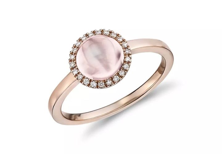 A round rose quartz cabochon ring accented by a diamond halo in a rose gold setting